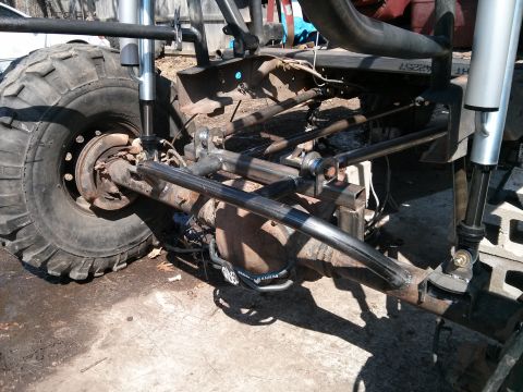 1986 Ford Bronco - Close-up view of a heavily modified off-road vehicle chassis, focusing on the suspension and large tire.