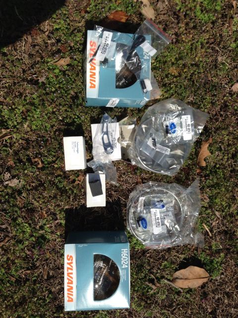 1979 Ford Bronco - Several Sylvania headlight boxes and other automotive parts are displayed on a grassy surface.