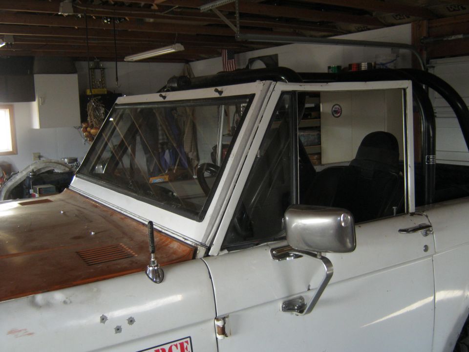 Front passenger side view of a white 1970 Ford Bronco with a black top and roll cage, parked inside a garage