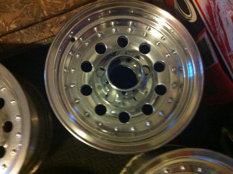 1992 Ford F-150 - Freshly polished aluminum truck wheel photographed face-on indoors, showing its mirror-bright simulated beadlock bolt ring, twelve oval ven…