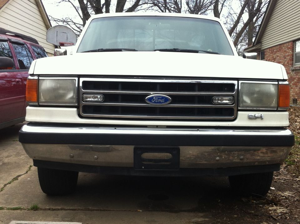 Front view of a white 1990 Ford F-150 parked in a driveway. Another vehicle is partially visible to the left