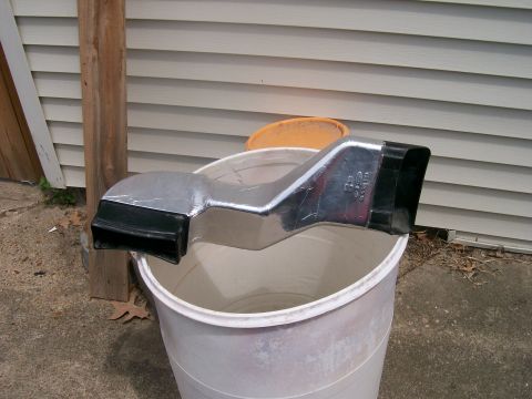 1990 Ford F-150 - A chrome air intake duct with black fittings sits in a white bucket, with a wooden post and siding in the background.