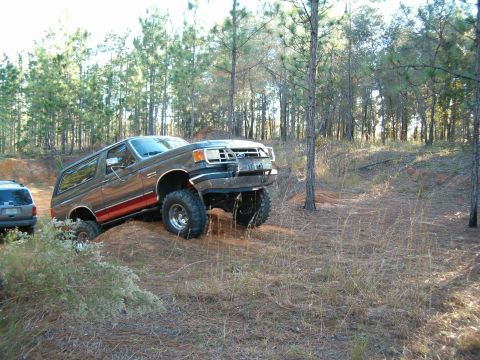1991 Ford Bronco - A lifted Ford Bronco navigates an off-road trail with another SUV visible in the background.