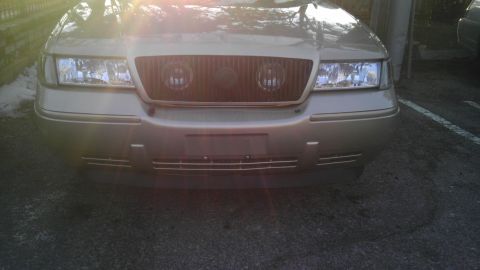 2000 Mercury Grand Marquis - The front of a gold 2000 Mercury Grand Marquis is visible, with its headlights and grille clearly displayed.