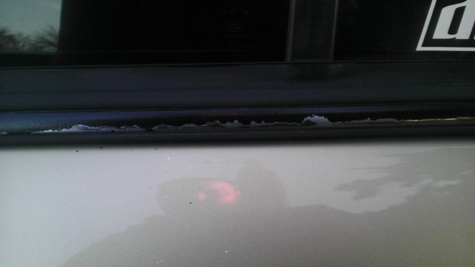 Peeling paint on a silver car door frame with a black trim piece above
