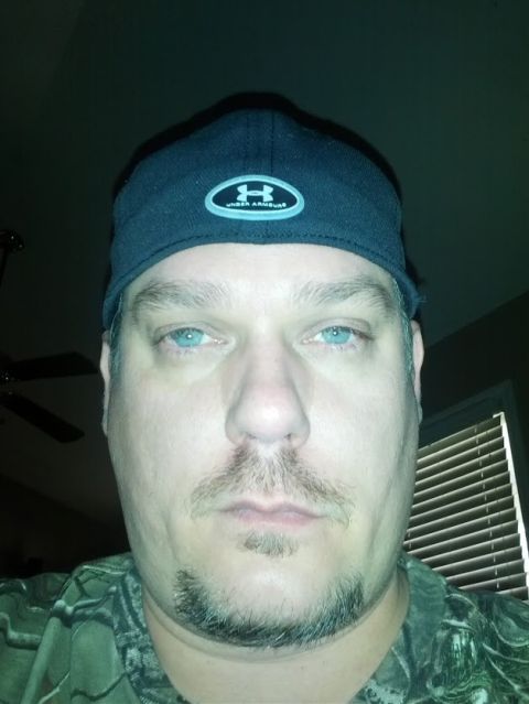 1979 Ford F-150 - A man with striking blue eyes is captured in a close-up selfie, wearing a baseball cap and camouflage clothing.