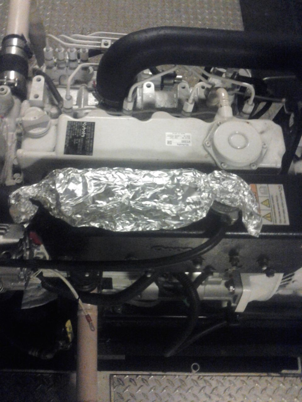 Engine block with aluminum foil covering part of it. Black hoses and white components are visible