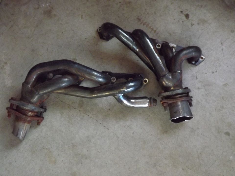 Two shorty exhaust headers with rusty collector flanges lying on a concrete floor