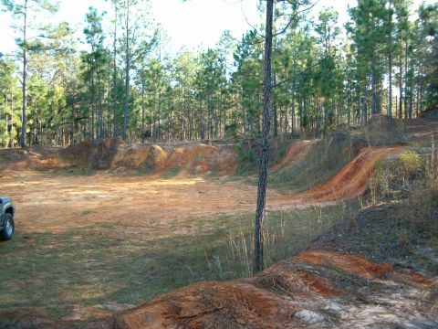 1991 Ford Bronco - A dirt track with mounds and jumps is shown in a wooded area with a vehicle partially visible on the left.