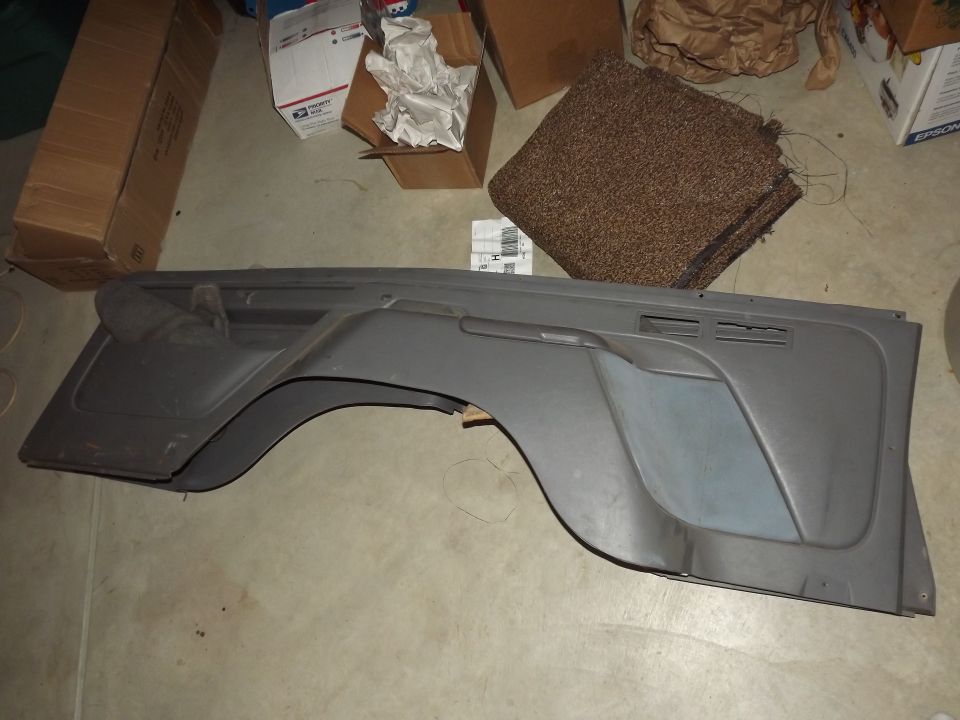 Gray interior door trim panels lying on a garage floor next to boxes and carpet