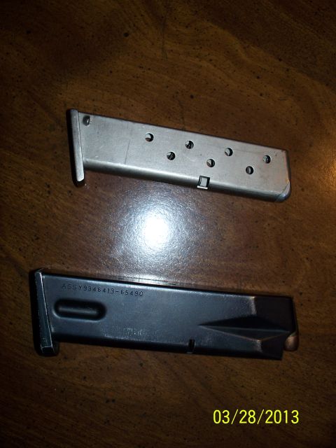 2000 Nissan Xterra - Two firearm magazines are shown on a wooden table. One is silver, the other is black with visible markings.
