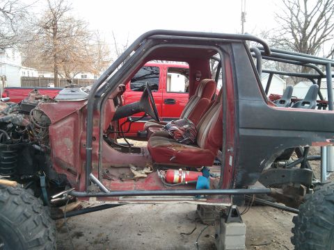 1986 Ford Bronco - This heavily modified SUV shows its interior and chassis, with a red pickup truck visible behind it.