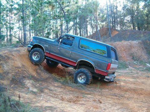 1991 Ford Bronco - A lifted Ford Bronco navigates an off-road trail with steep inclines and loose dirt.