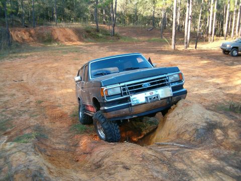 1991 Ford Bronco - 1991 Ford Bronco tackles a challenging off-road course with a rock obstacle.