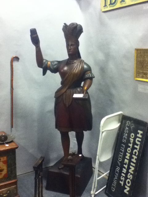 2006 Ford E350 - A wooden statue of a woman, possibly an advertisement, stands with a cane and a sign for an optician in the background.