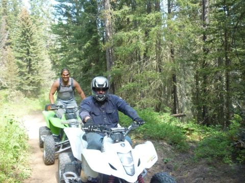 2006 Ford E350 - Two individuals enjoy a ride on ATVs through a forest trail, surrounded by lush greenery and tall trees.