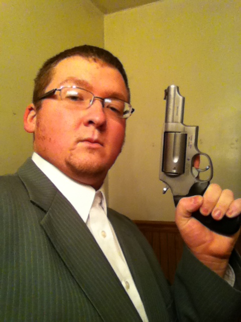 2006 Ford E350 - A man in a suit and tie poses for a selfie while holding a revolver.