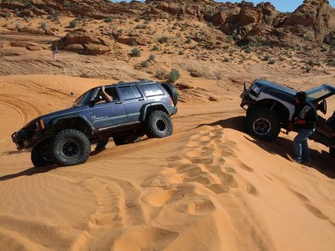 1994 Ford Bronco - Two off-road vehicles navigate sandy terrain in a desert landscape.