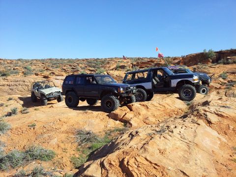 1994 Ford Bronco - Several off-road vehicles are parked on a rocky incline in a desert landscape.