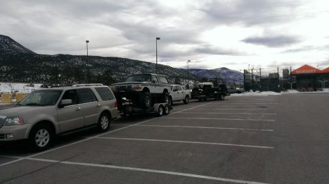 1994 Ford Bronco - A lifted Ford Bronco is transported on a trailer, with a silver SUV leading the way.