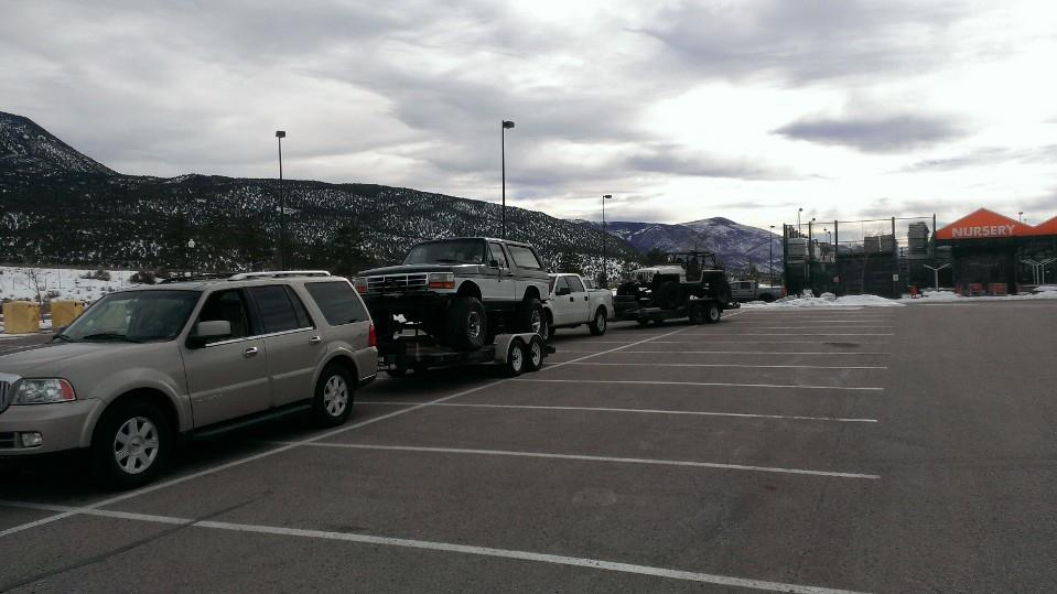 Two-tone lifted Ford Bronco on a trailer, towed by a silver SUV
