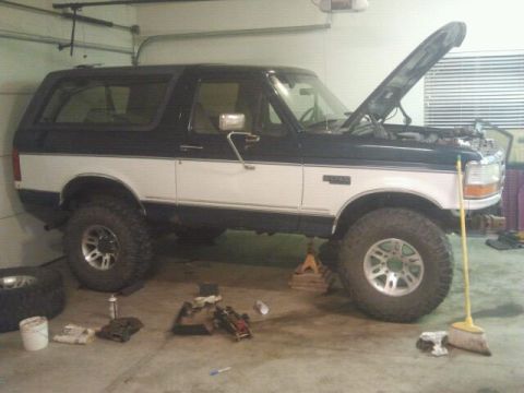 1994 Ford Bronco - This two-tone Ford Bronco is in a garage, elevated on jack stands with its hood open.