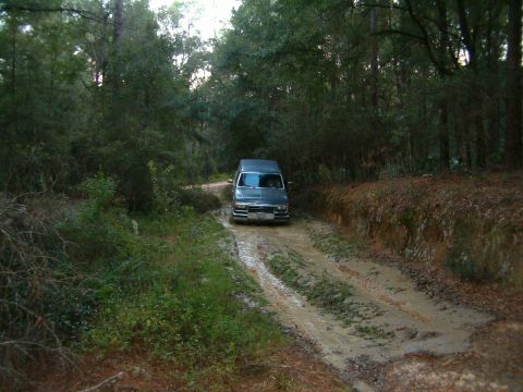 1991 Ford Bronco - Van navigates a muddy track in a forest setting.