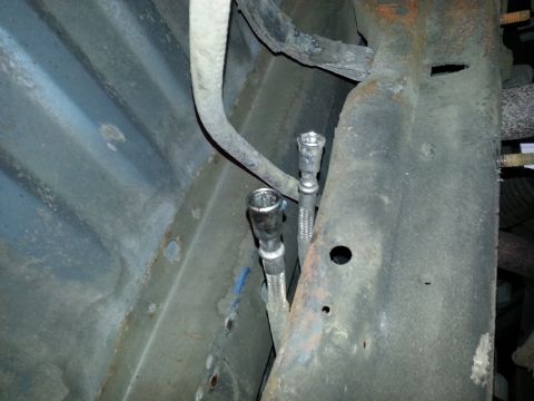 1994 Ford Bronco - Close-up of flexible fuel lines attached to a vehicle's undercarriage.