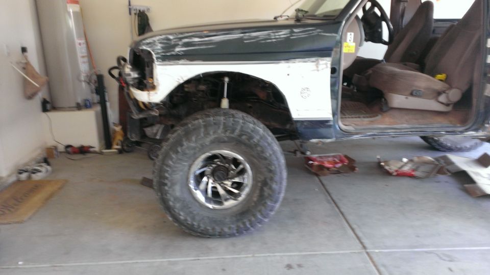 Dark green and white Ford Bronco in a garage, front passenger side visible, missing front fender and headlight