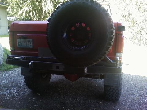 1989 Ford Bronco - Rear view of a red SUV with a spare tire on the back and a custom bumper.