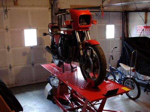 2008 Ford Crown Victoria - A red motorcycle is elevated on a red hydraulic lift inside a garage, with a bicycle visible in the background.