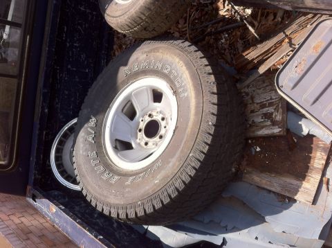 1991 Ford Bronco - Several tires and wheels are stored in the cargo area of a vehicle, with visible text on one tire.