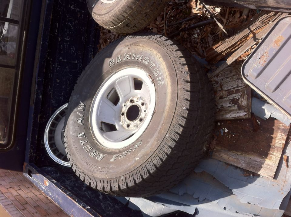 Tires and wheels piled in the bed of a dark-colored truck. One tire has 'REMINGTON' and 'BRUTE A/W' visible