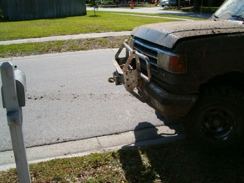 1991 Ford Bronco - Mud-covered 1991 Ford Bronco front end with brush guard and tow hitch visible.