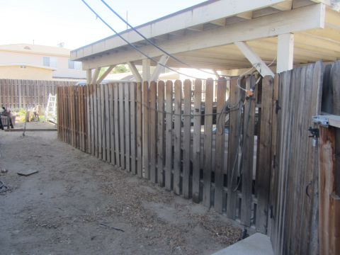 1968 Ford Mustang - Backyard view showing a wooden fence, a carport structure, and some items stored in the yard.