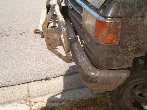 1991 Ford Bronco - The front of a heavily soiled truck is shown parked on the side of a road, with mud caked on the bumper and fender.