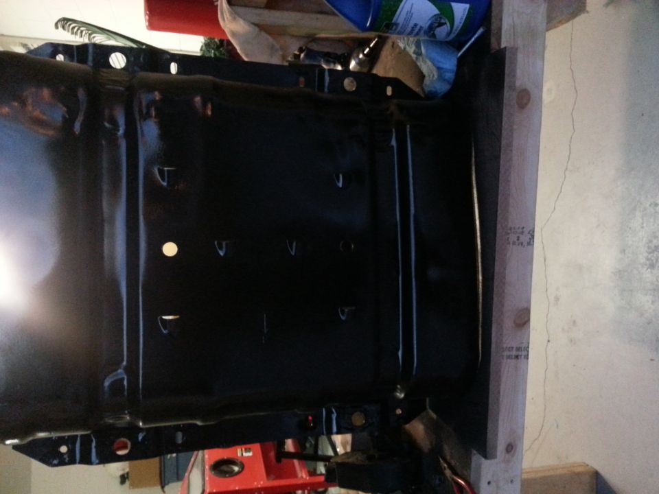 Black metal part with holes, mounted on wood, with a red object below