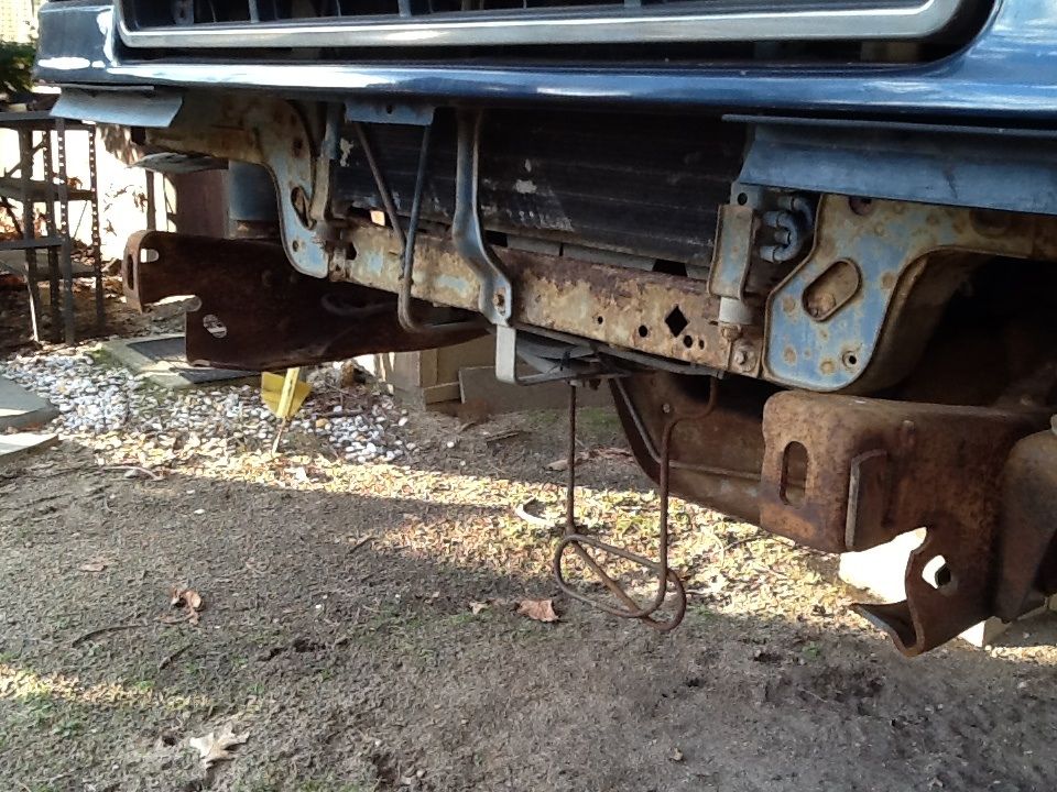 Front end of a vehicle with rusted bumper mounts and frame components visible