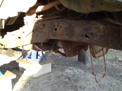 1989 Ford Bronco - The heavily rusted frame and suspension components of a vehicle are visible, supported by jack stands.