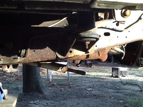 1989 Ford Bronco - Close-up view of heavily rusted vehicle frame and suspension parts, with an exhaust pipe hanging low.
