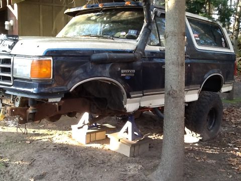 1989 Ford Bronco - A dark blue and white Ford Bronco is shown on jack stands with a snorkel intake and lifted suspension.