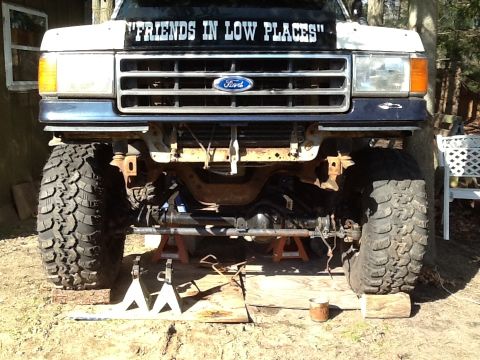 1989 Ford Bronco - Front view of a Ford Bronco on jack stands, showing the suspension and large off-road tires.