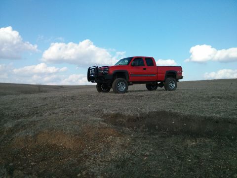 1986 Ford Bronco - A red pickup truck is parked on a barren, grassy hill with a bright blue sky and scattered clouds above.
