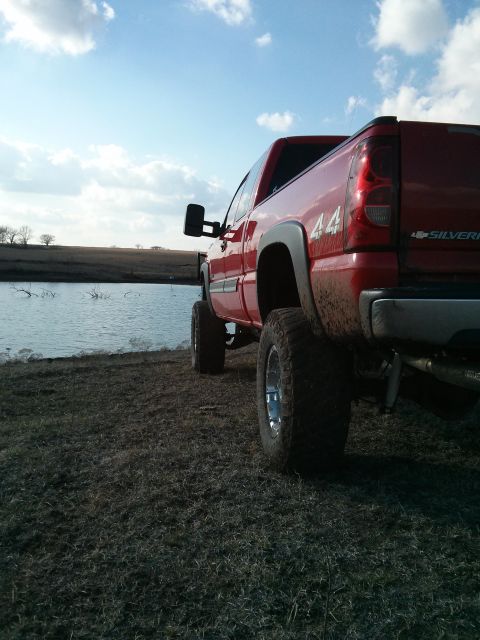 1986 Ford Bronco - A red pickup truck sits on a grassy bank next to a calm body of water under a cloudy sky.