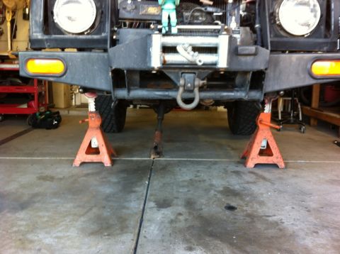 1987 Suzuki Samurai - The front axle and suspension of a 1987 Suzuki Samurai are visible as the vehicle is supported by jack stands.