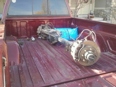 1994 Ford Bronco - Rear axle assembly and other items loaded in the bed of a red pickup truck.