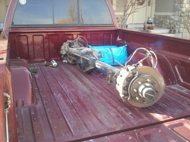 Rear axle assembly with brake rotors and calipers, a blue bag of salt, and a can in a red pickup truck bed
