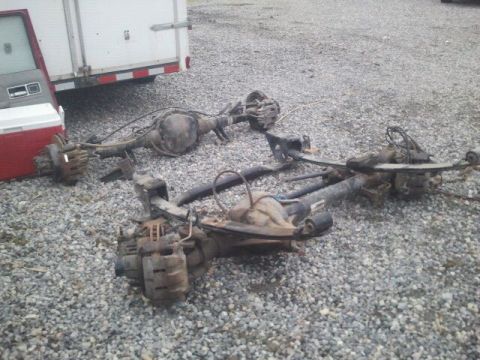1994 Ford Bronco - Two vehicle rear axles with brake components and leaf springs are visible on a gravel surface.