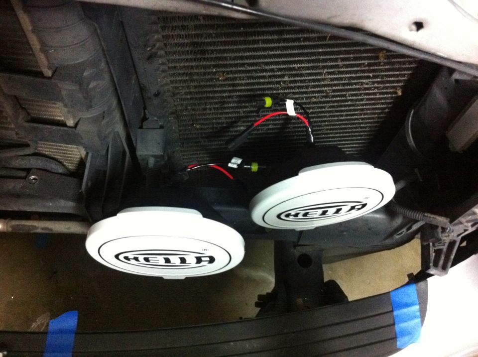 Two Hella HID lights mounted in front of a vehicle's radiator, with wiring visible