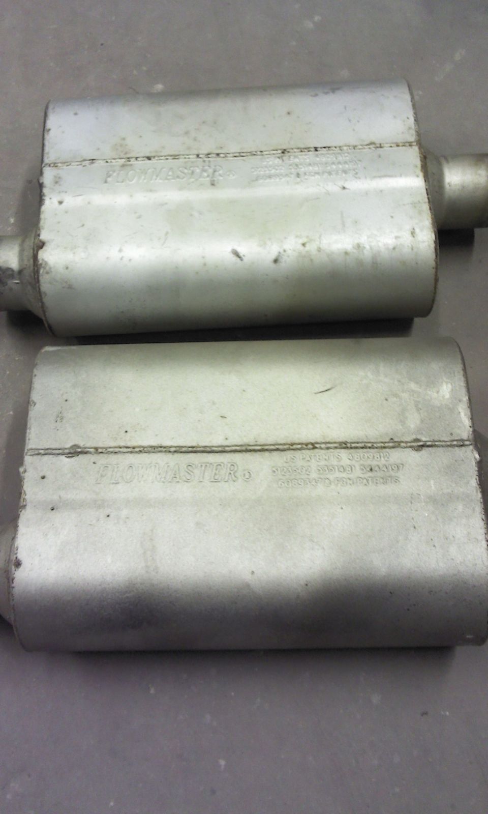 Two silver Flowmaster mufflers side-by-side on a gray surface